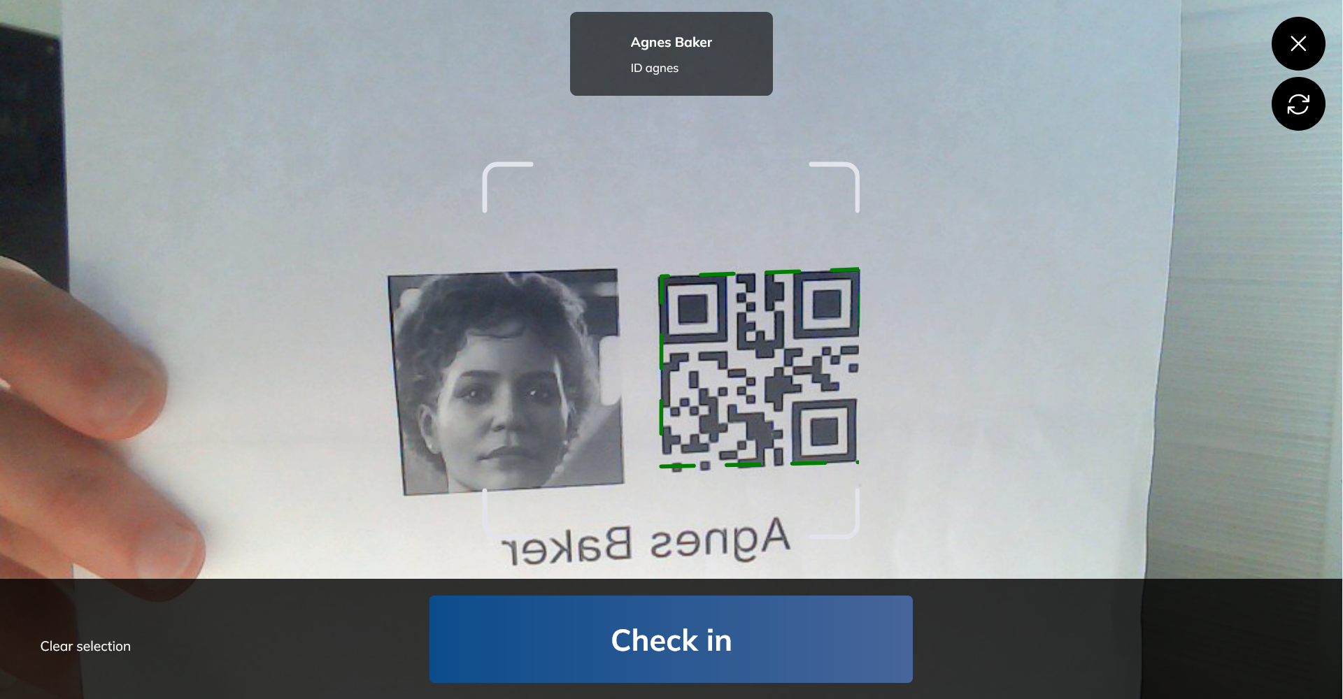 The camera view scanning a printed badge, with the matched person's name at the top and a Check in button across the bottom.